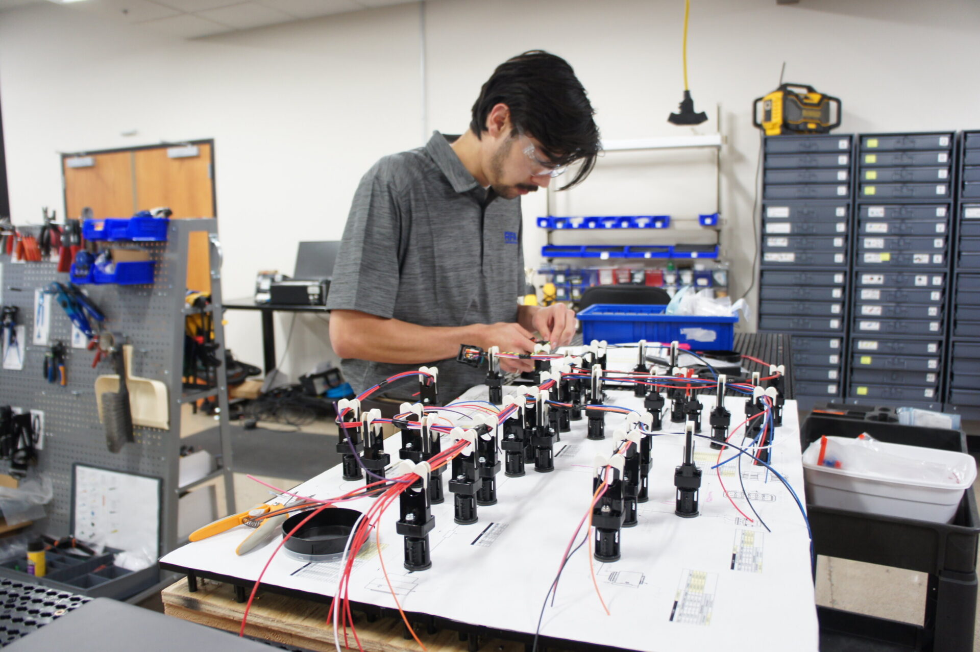 Technician assembling custom wire harness prototype with electronic components on workbench in engineering lab.