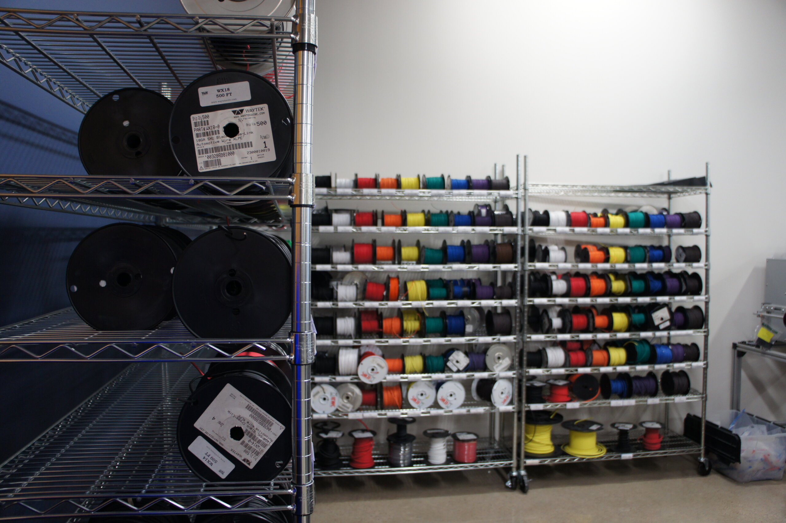 Industrial storage area with metal shelves holding large black spools on the left and racks of colorful thread spools on the right.