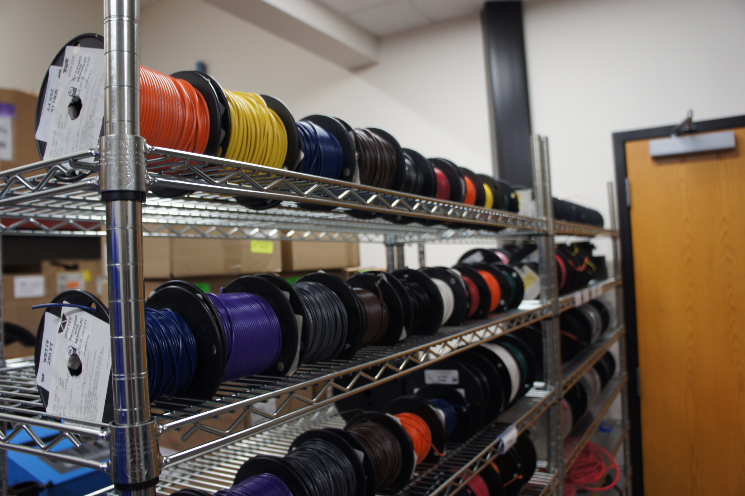 Spools of colored cables on metal shelving in a workshop or storage room.