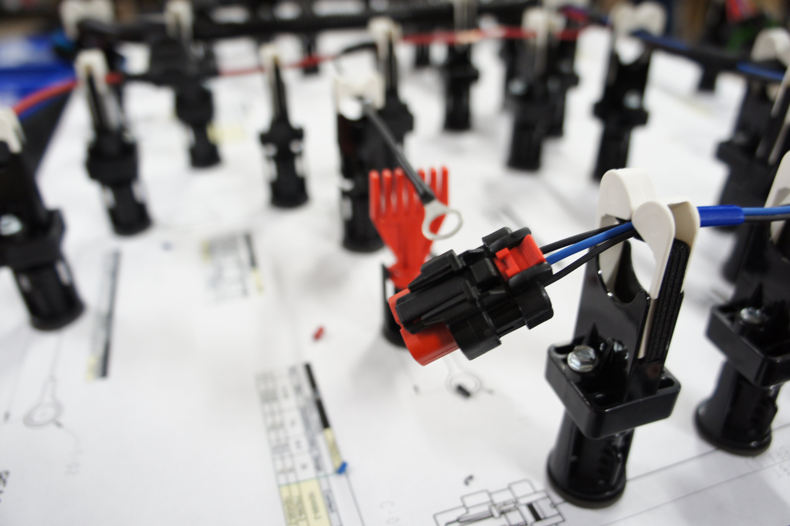 Close-up of a robotic kit with black frame, red connectors and blue cables on a white surface with a schematic in the background