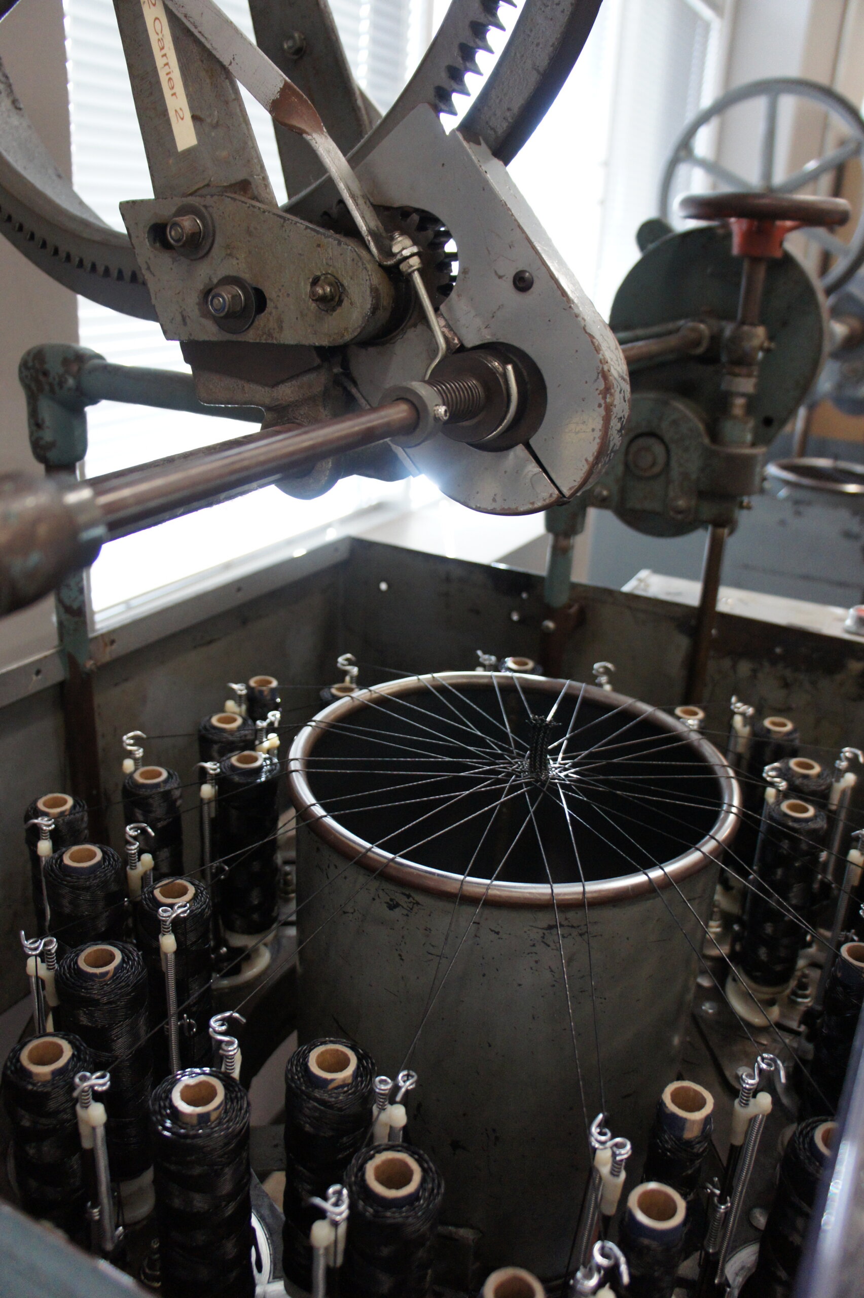 Industrial wire-winding machine with a large circular gear and many spool bobbins arranged around a central cylinder, wires feeding into a central coil.