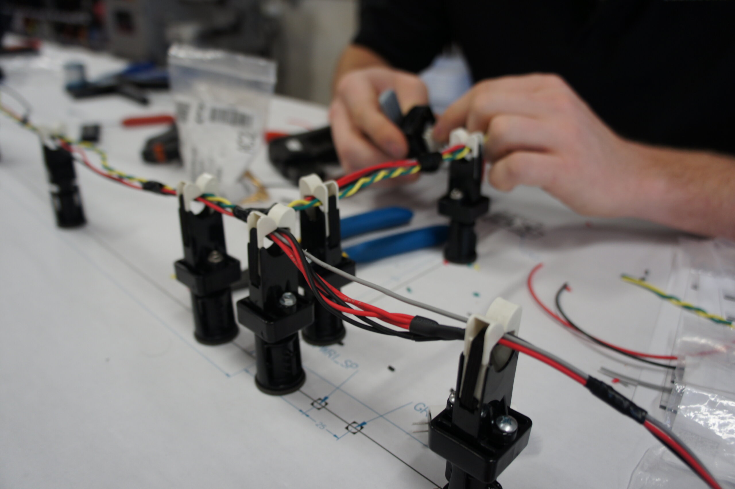 Hands wiring a small robotic frame on a white workbench, connectors and multicolored wires visible (blurry photo).