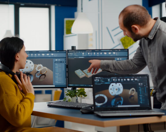 RFA Engineering team members collaborating on a 3D design project, analyzing mechanical components displayed on multiple screens.