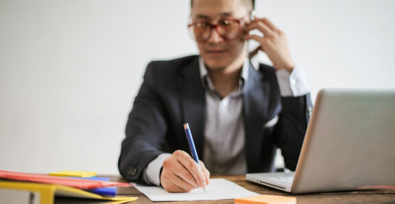 A business professional on the phone while taking notes, highlighting the significance of clear client communication in delivering quality service.
